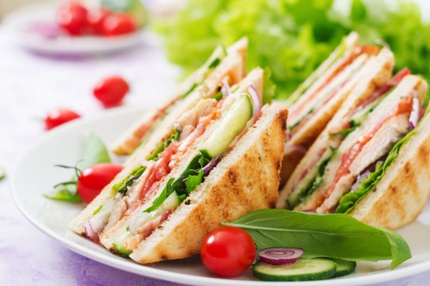 Sandwiches cut into triangles. There are also tomatoes, cumber and salat on the plate.
