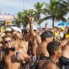 A large group of people cheering in the sun in bathing suits with palm trees in the background.