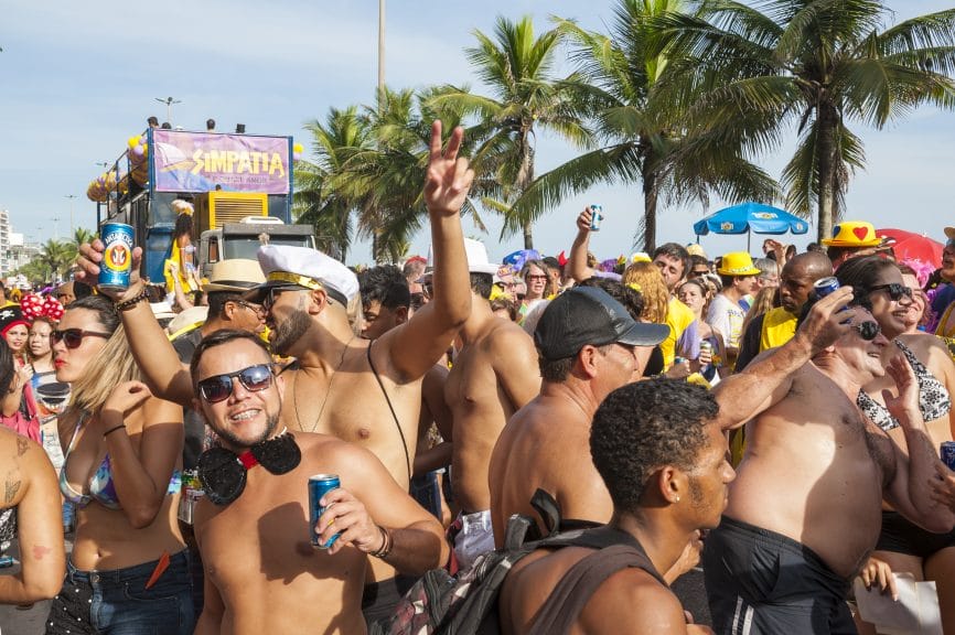 A large group of people cheering in the sun in bathing suits with palm trees in the background.