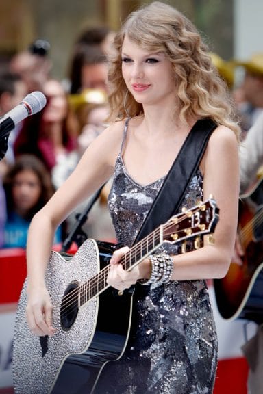 Taylor Swift performing with an acoustic guitar.