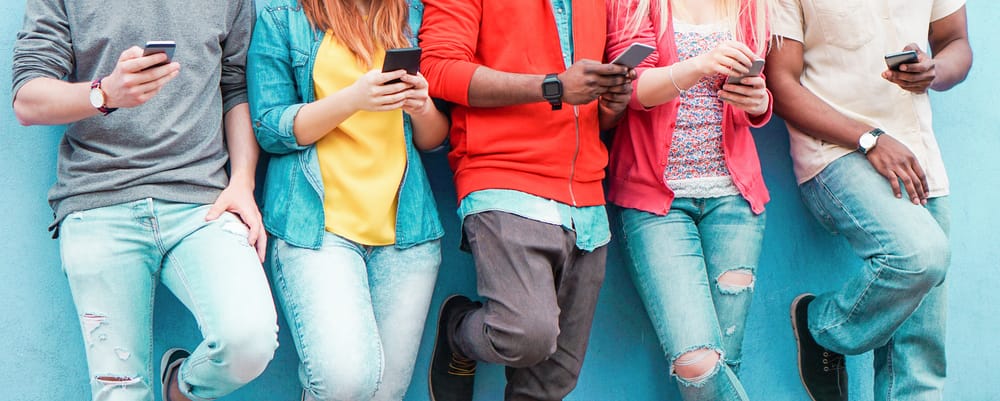 A group of teenagers against a wall on their phones watching videos and scrolling through social media