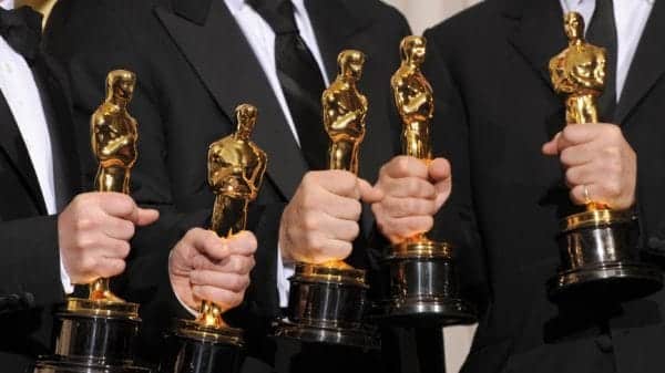 Five gold Oscar statues being held