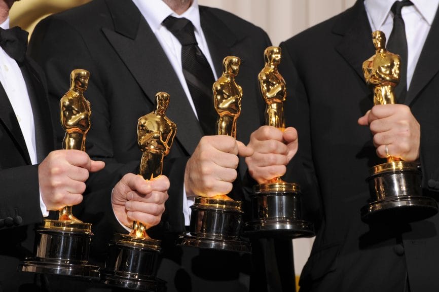 Five gold Oscar statues being held