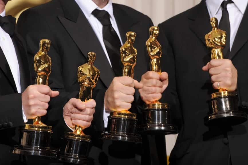 Five gold Oscar statues being held