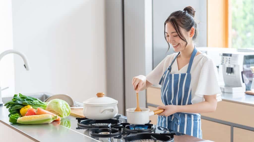 A woman in a blue striped apron mixing a pot of food on the stove
