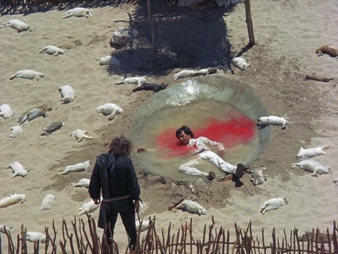 El Topo (Alejandro Jodorowsky) stands the man he shot in a desolate, massacred town.