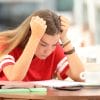 Stressed out girl in high school, holding her head in her hands while looking down at homework.