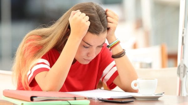 Stressed out girl in high school, holding her head in her hands while looking down at homework.