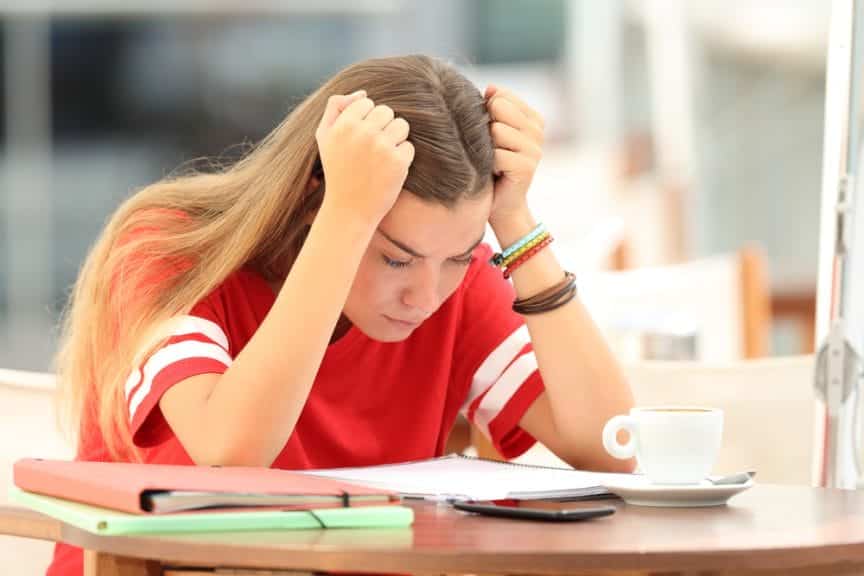 Stressed out girl in high school, holding her head in her hands while looking down at homework.