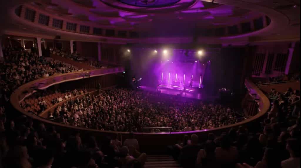 Crowd of people and purple lights on stage.