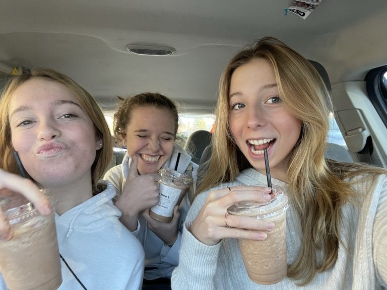 Three girls in the car drinking coffee.