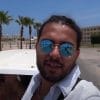 An Arabian man in a white shirt and sunglasses behind a desert backdrop