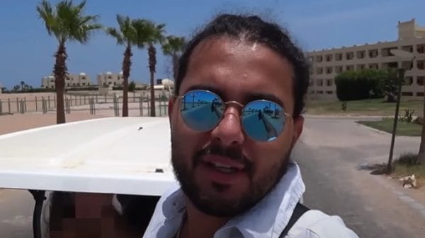 An Arabian man in a white shirt and sunglasses behind a desert backdrop