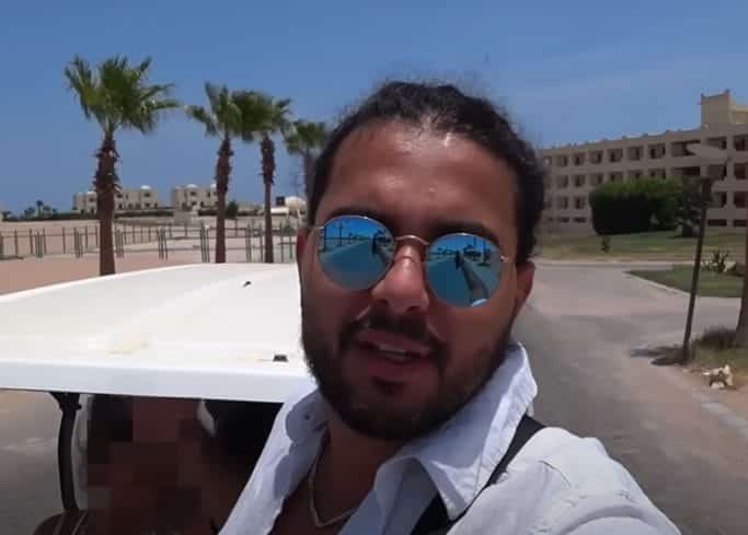 An Arabian man in a white shirt and sunglasses behind a desert backdrop