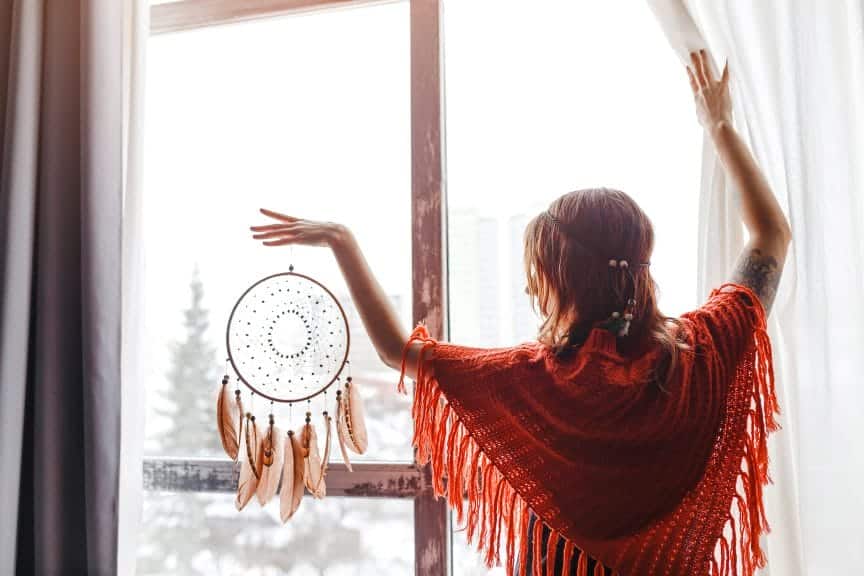 A woman holding a dreamcatcher at a window.