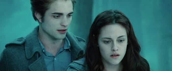 Edward Cullen (Robert Pattinson) standing behind Bella Swan (Kristen Stewart) in the woods.
