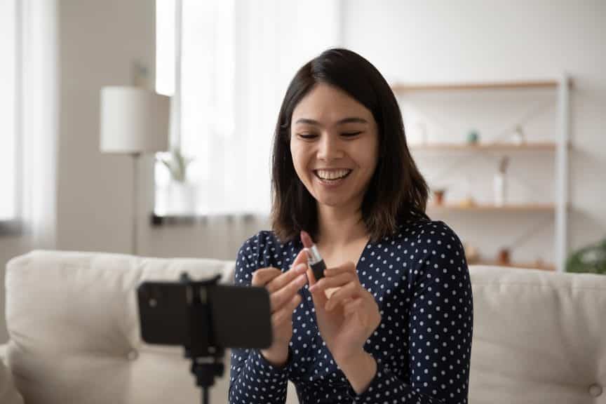 A woman holding a new lipstick and smiling as a part of consumer culture.