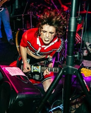 A musician plays guitar dressed in an androgynous punk-rock costume