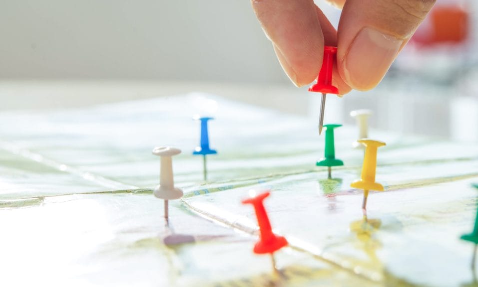 A zoomed in map with a hand placing numerous push pins.