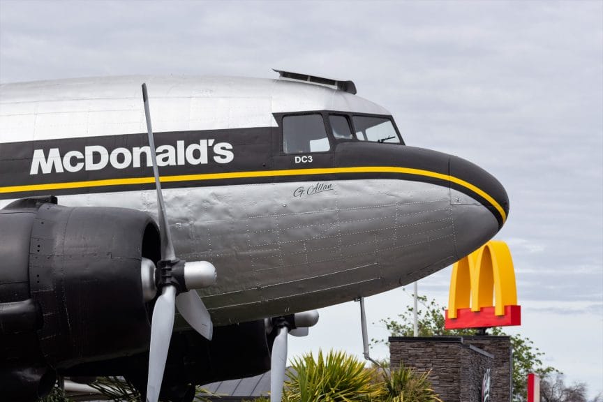 The nose end of an aeroplane that is black and silver with a yellow stripe and has McDonald's written on it