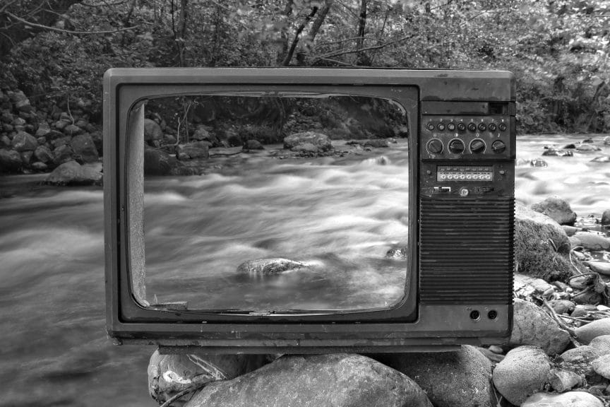 Retro TV on river shore near forest

