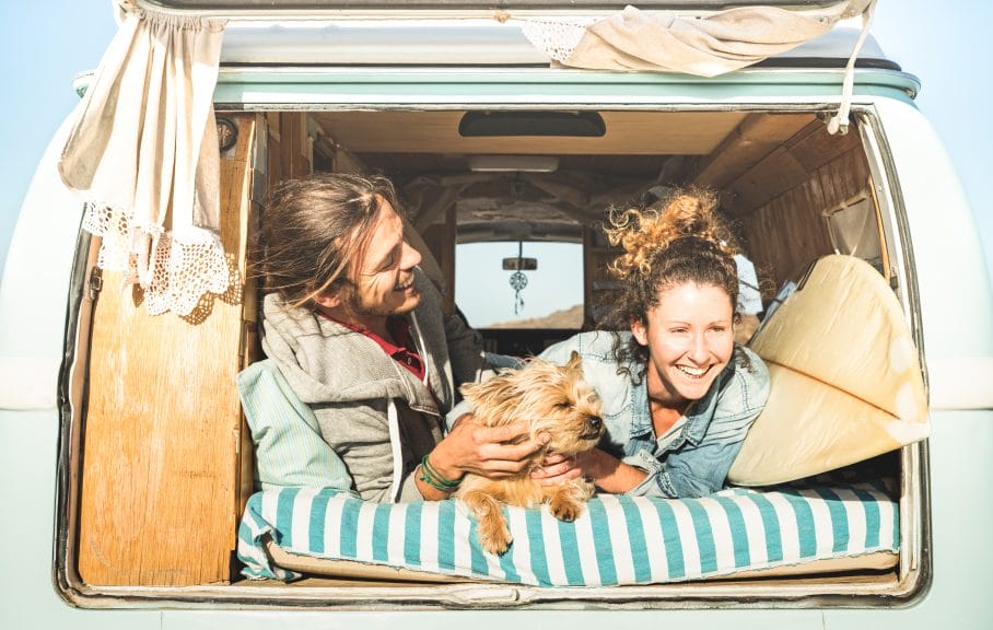 Hipster couple with cute dog traveling together in vintage minivan transportation.