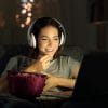 woman watching something on her laptop with headphones and a popcorn bucket.