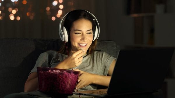 woman watching something on her laptop with headphones and a popcorn bucket.