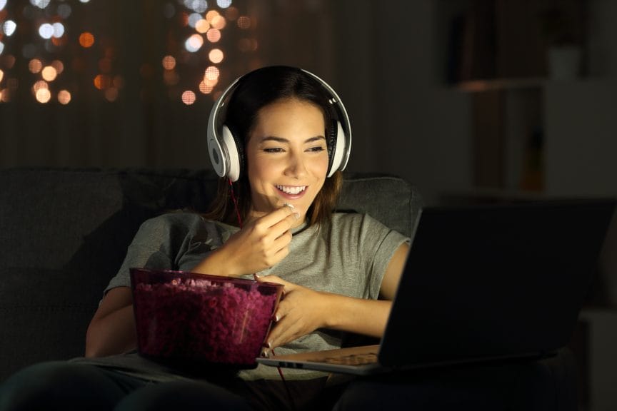 woman watching something on her laptop with headphones and a popcorn bucket.