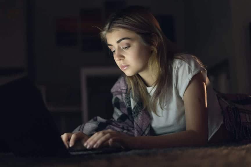 teenage girl watching a video or working on her laptop at night in the dark. The laptop screen lights up her face.