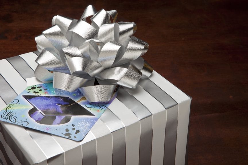 A gray/silver and white gift box with a card on top with a graduation cap on it. 