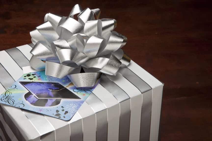 A gray/silver and white gift box with a card on top with a graduation cap on it.