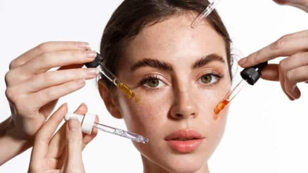 A woman with peoples hands around her putting serums on her face