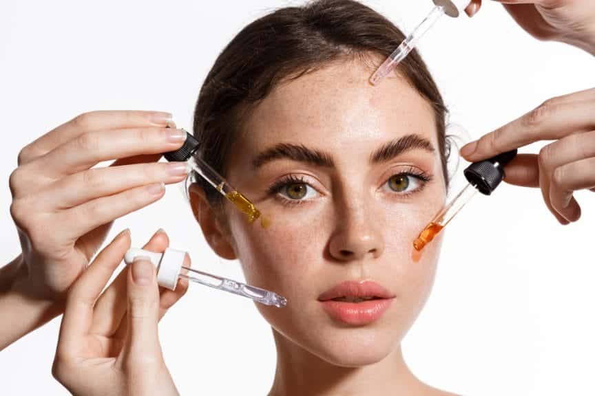 A woman with peoples hands around her putting serums on her face