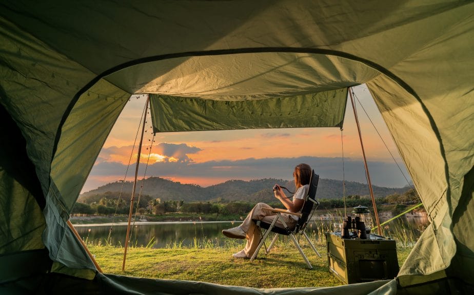 Woman sat in camp chair in front of tent, overlooking lake scenery 