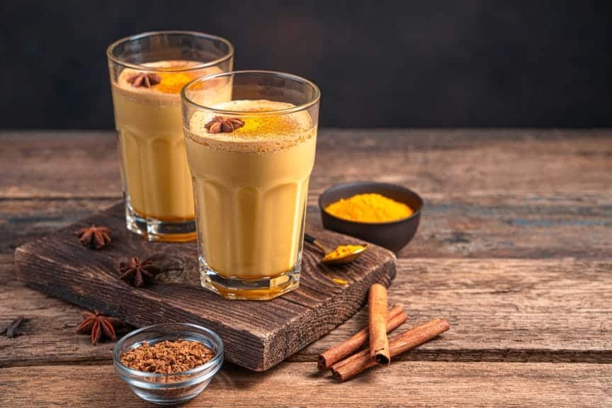 coffee alternative golden milk in two glasses with cinnamon and turmeric cloves