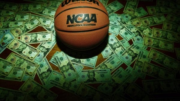A basketball in money. College athletes are dealing with the pressure that comes with sports betting.