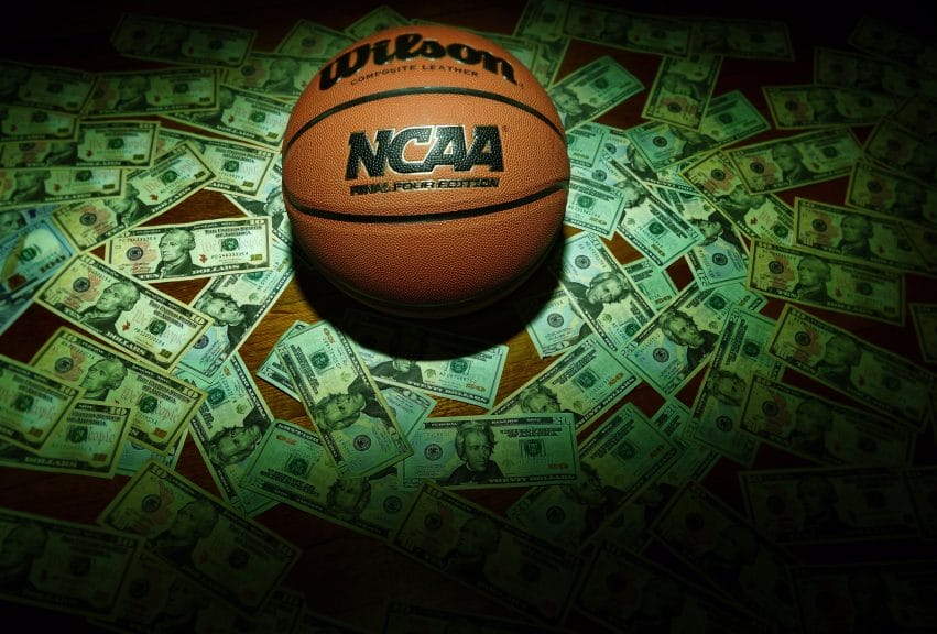 A basketball in money. College athletes are dealing with the pressure that comes with sports betting.