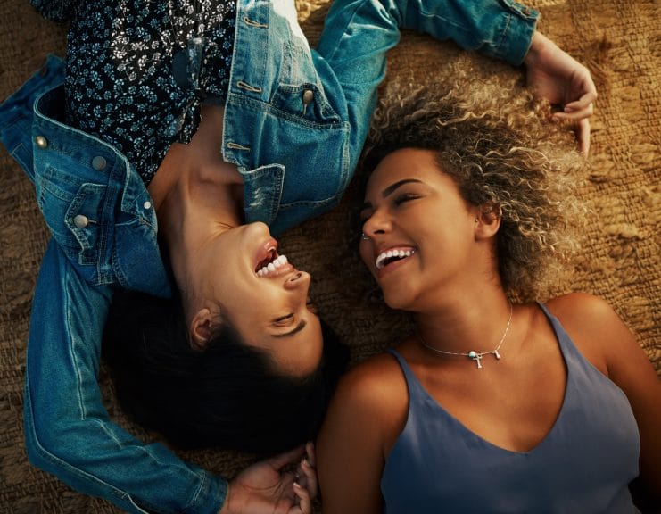 High angle shot of two attractive young girlfriends smiling at each other while lying down at a park.