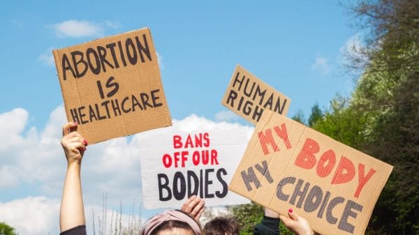 Four signs are up in the air reading: "abortion is healthcare" "bans off our bodies" "human right" "my body my choice"