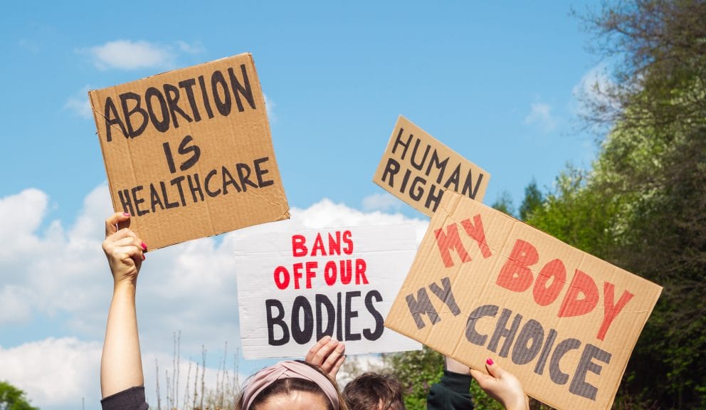 Four signs are up in the air reading: "abortion is healthcare" "bans off our bodies" "human right" "my body my choice"