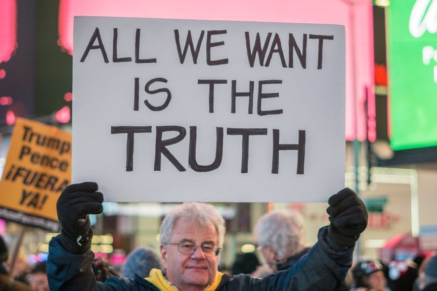 An old man holding a sign that advocates for truth in the middle of a protest. 