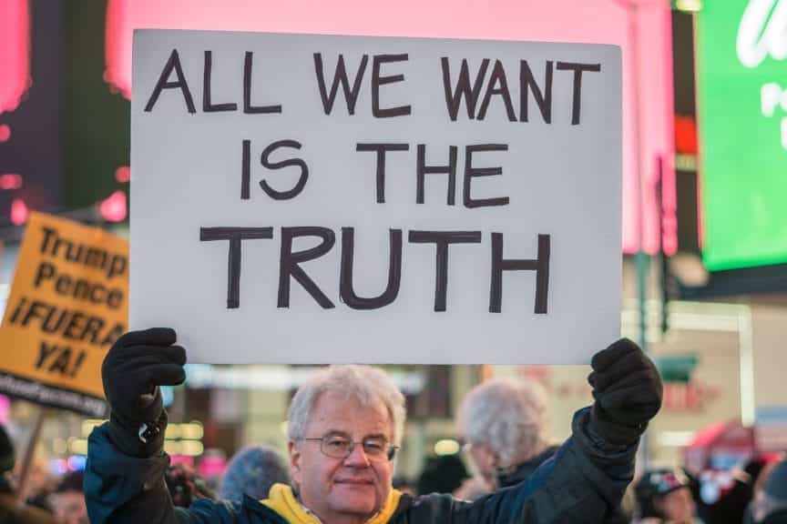 An old man holding a sign that advocates for truth in the middle of a protest.