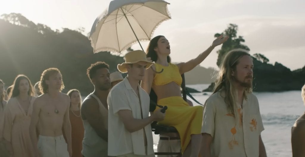 Lorde is being carried upon a chair on the beach.