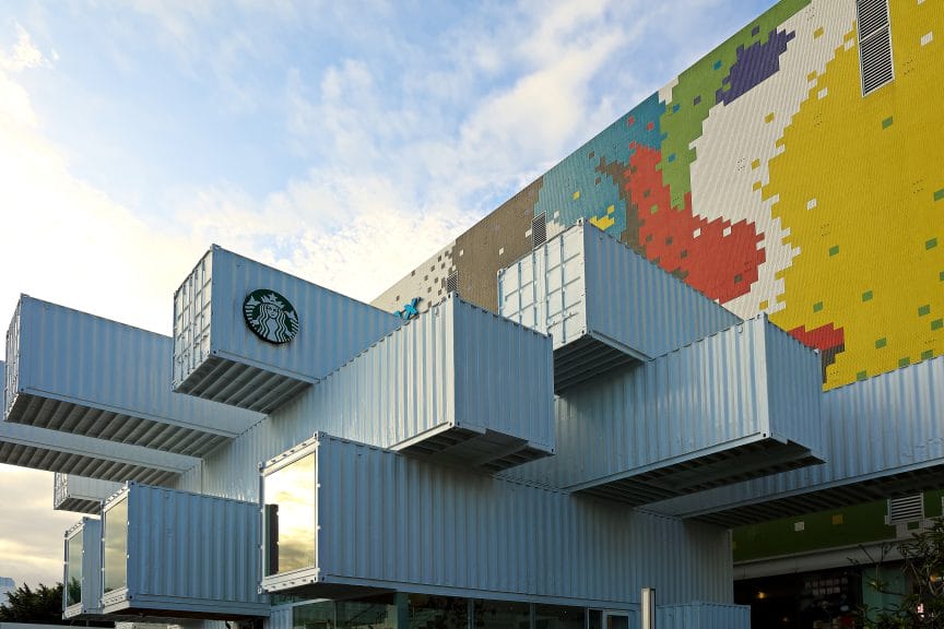 Six white shipping containers stack at different angles with a Starbucks logo on the side.