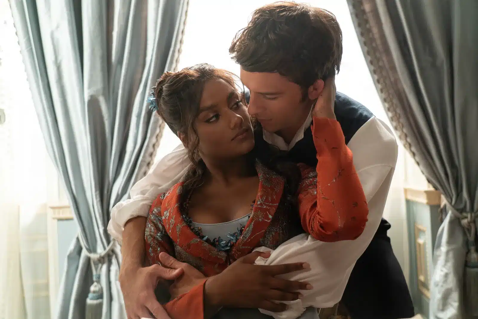 Viscountess Kate, beautiful young woman wearing an orange dress is hugged from behind by Viscount Anthony, a young man in a white shirt and blue vest.
