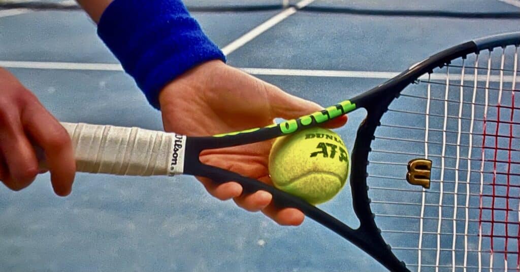 A man holding a tennis racquet, with a tennis ball in its throat.