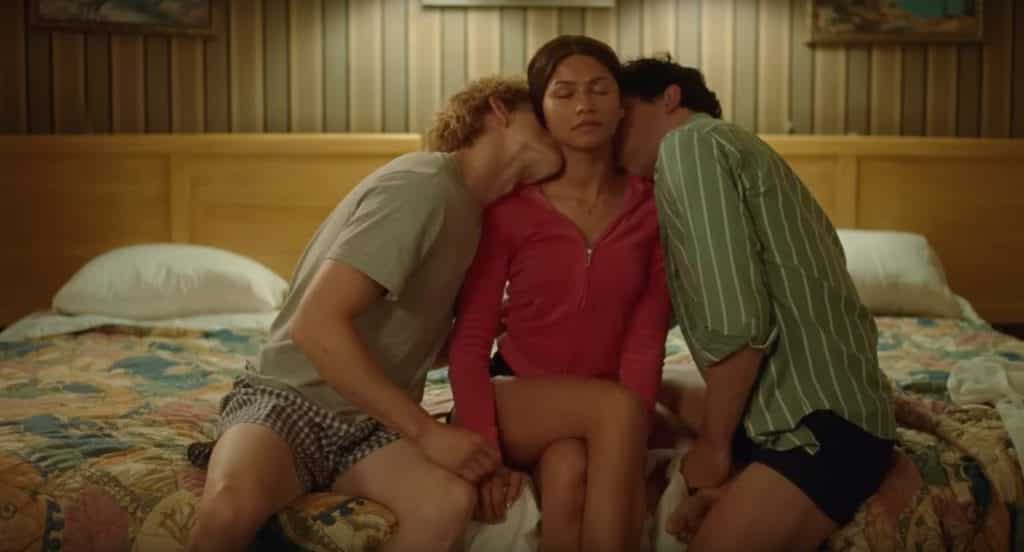 A man on the left-hand side of a woman, kissing her neck, and a man on her right-hand side, kissing her neck.