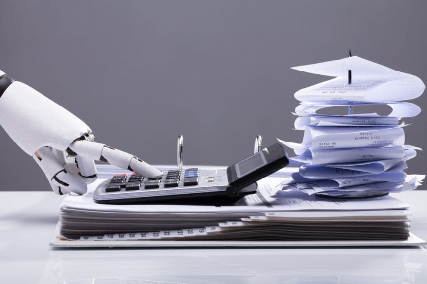 A robot hand typing into a calculator over documents and folded up receipts, doing taxes.