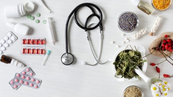 Western medicine on one half of the image and herbal remedies not he other with a stethoscope in the middle.